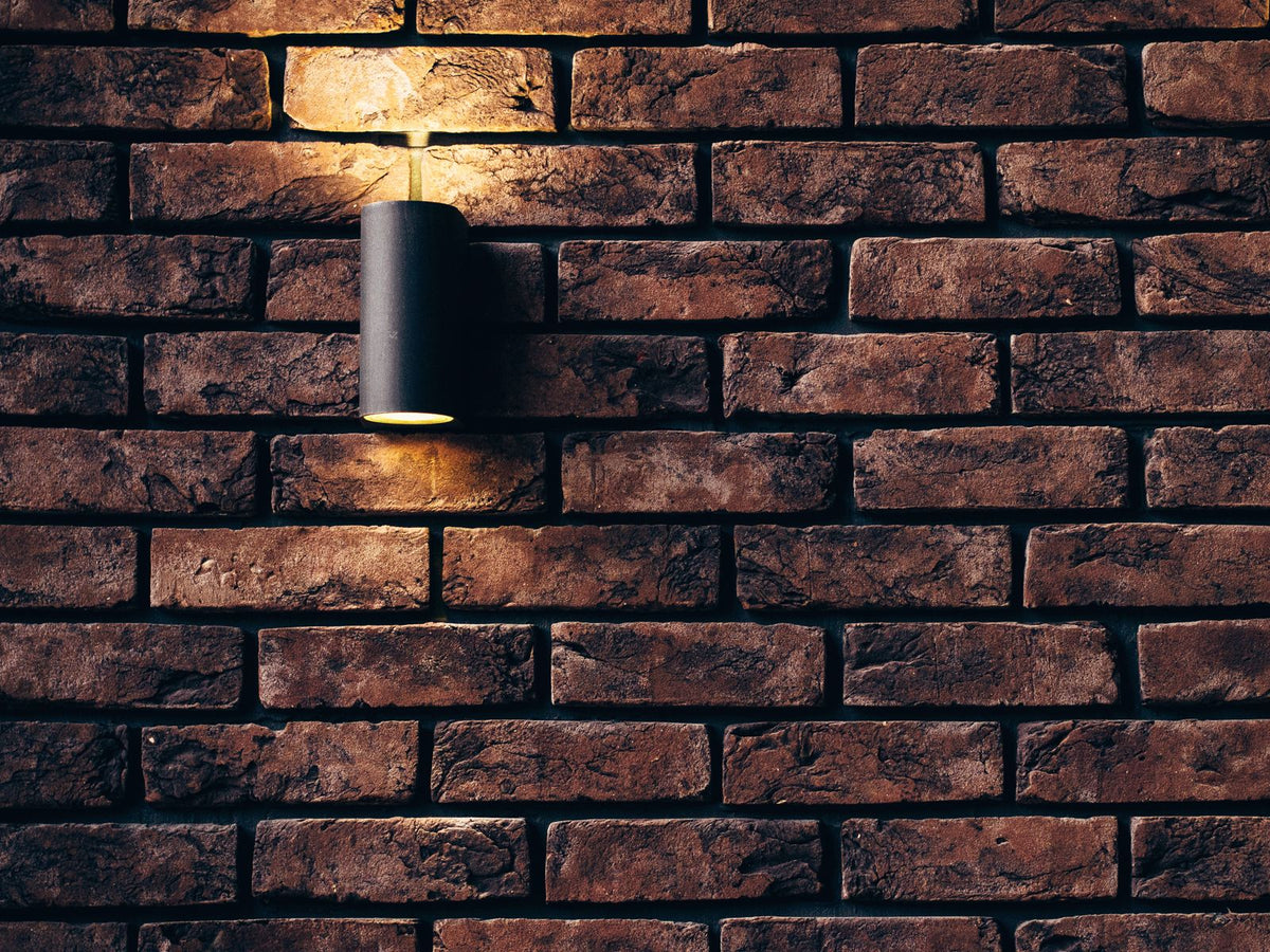 Black tubular wall sconce mounted on a brick wall
