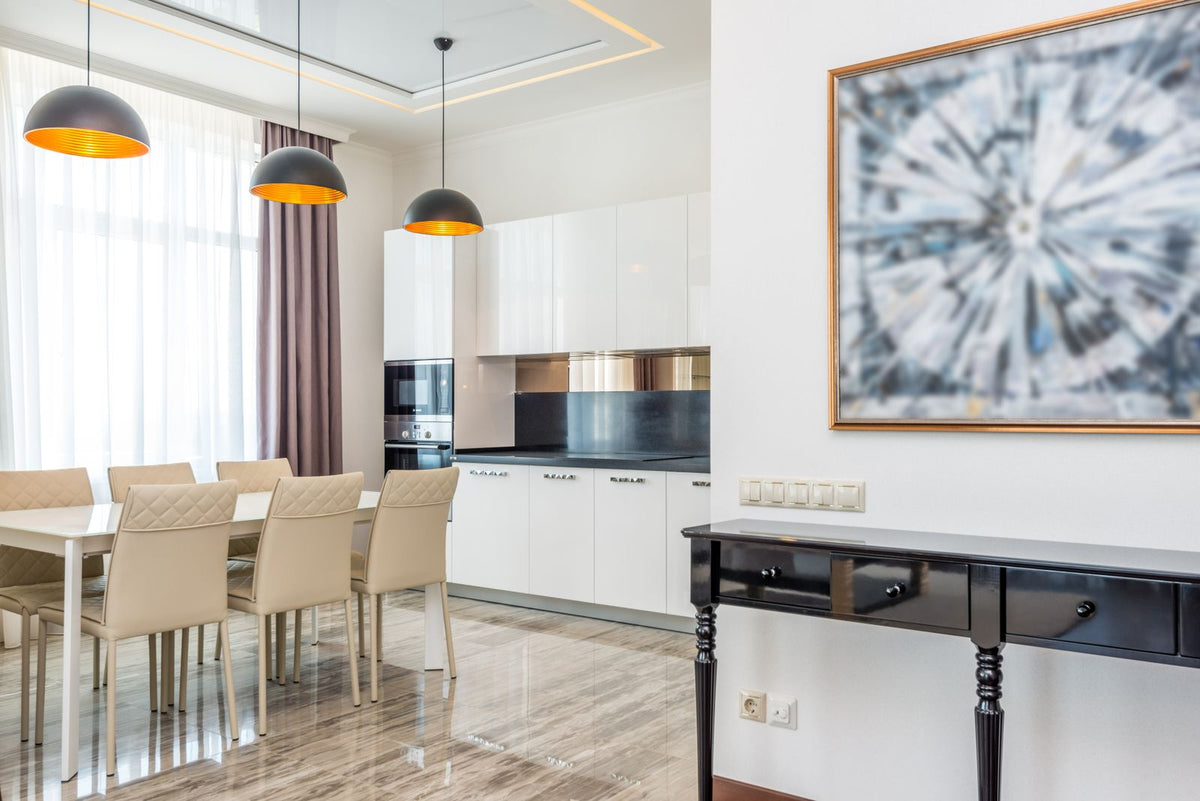 Dining room with three pendant lights over the table and a white kitchen behind