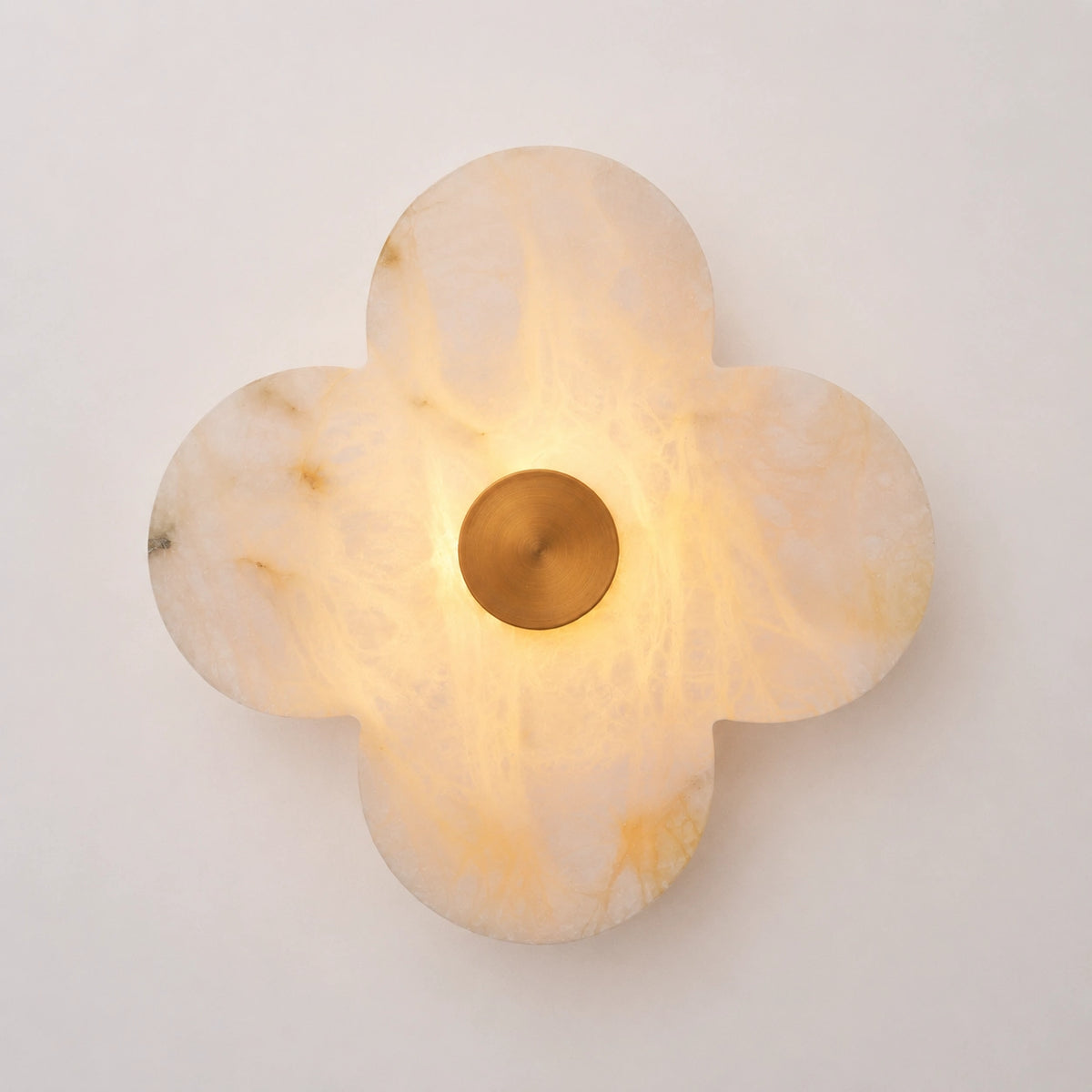 The Petalo alabaster clover sconce lit, glowing warm amber