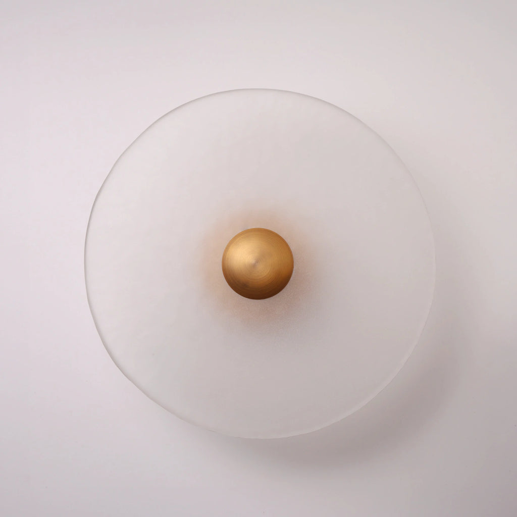 The Orbis frosted glass disc wall sconce in brass, lit with warm halo