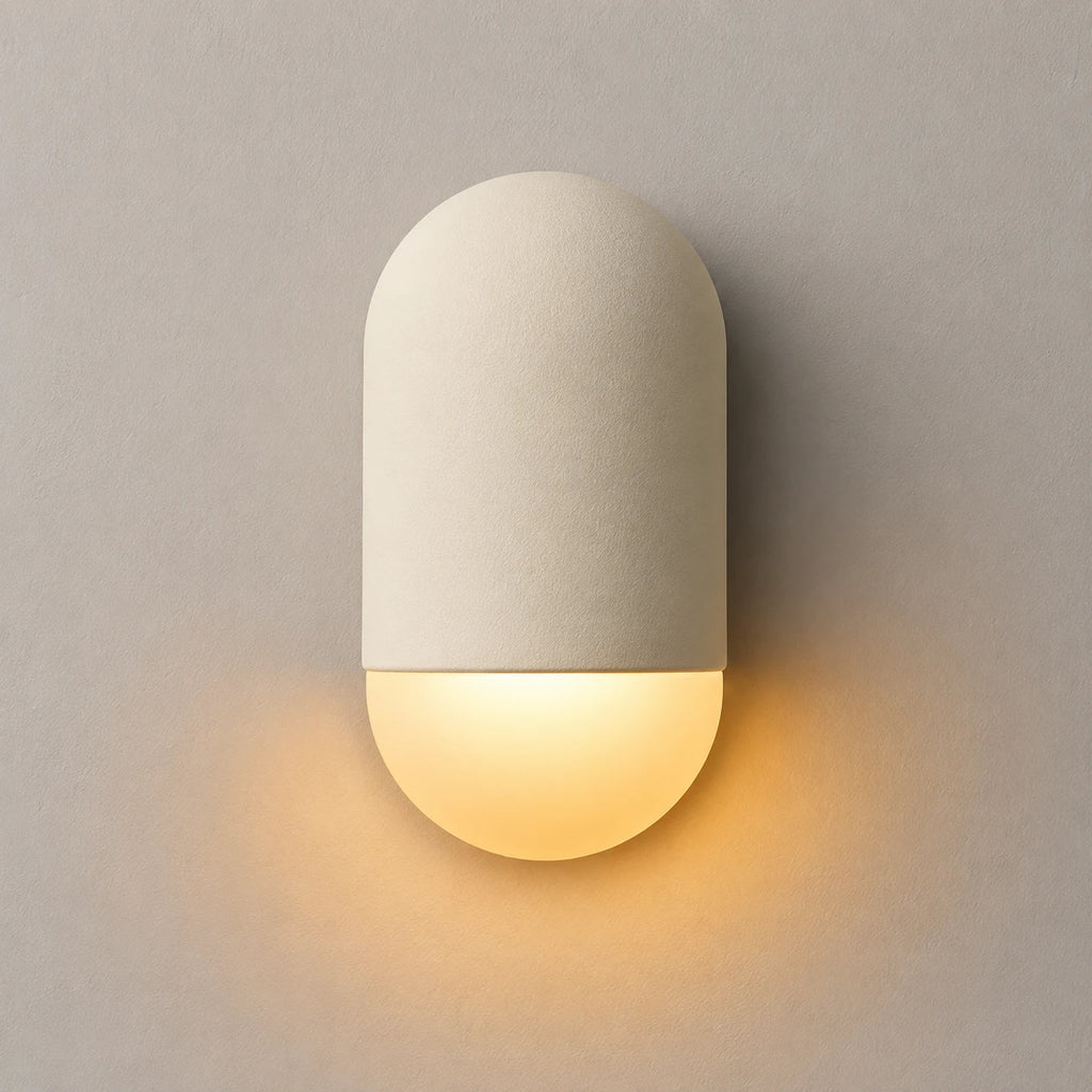 The Capsule ceramic wall sconce lit with warm downward glow