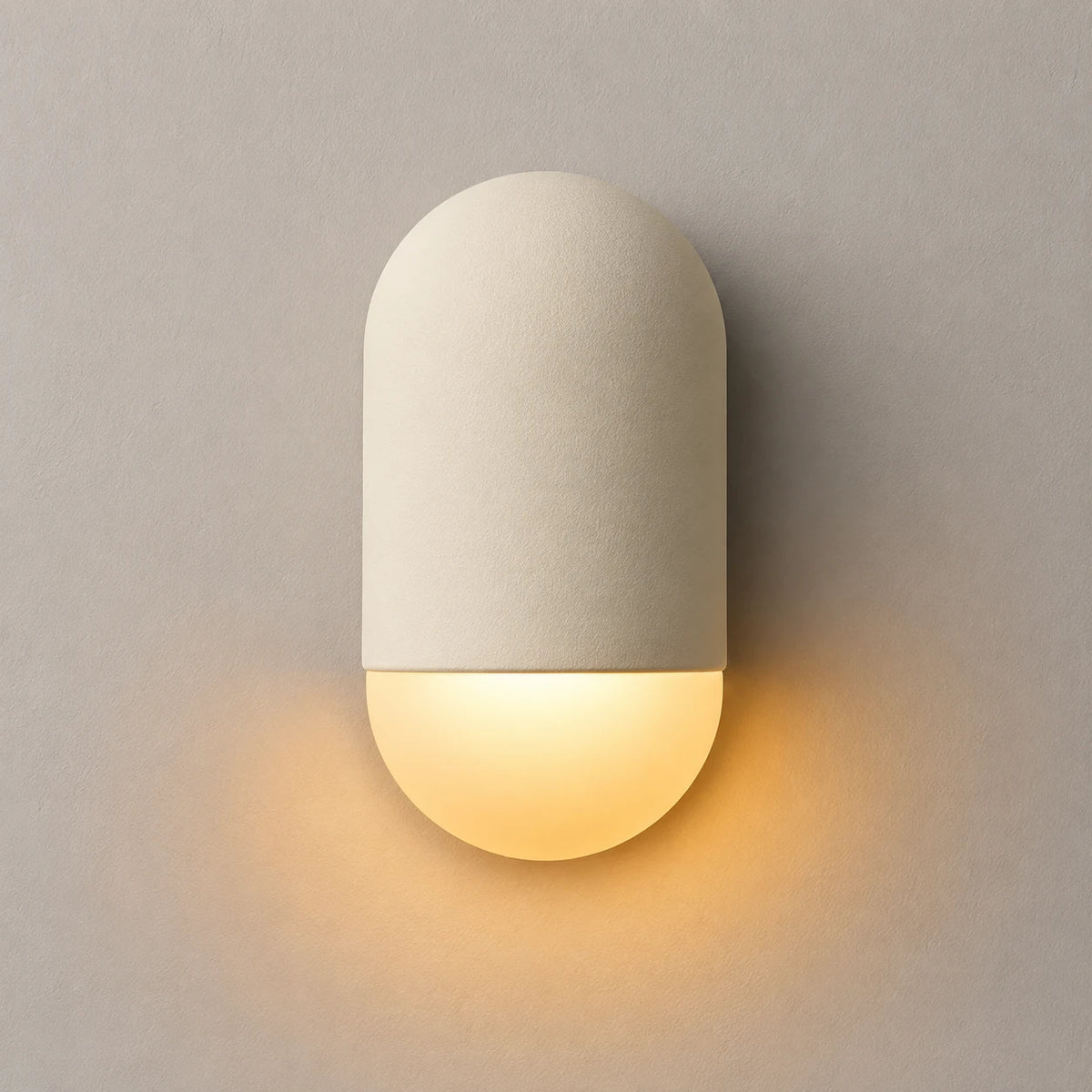 The Capsule ceramic wall sconce lit with warm downward glow